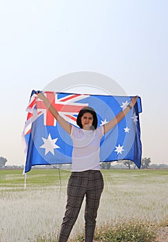 pretty lady is holding Australia flag in her hands and raising to the end of the arm at the back on nature view background