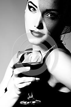 Pretty lady inhat with veil holding glass of wine, retro glamour beauty portrait. Beautiful woman with perfect makeup