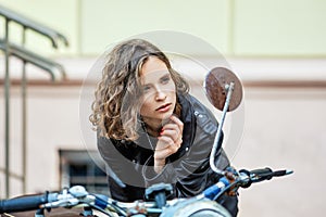 Pretty lady in leather coat and wild curly hair looking to rer view mirror of old vintage motorbike