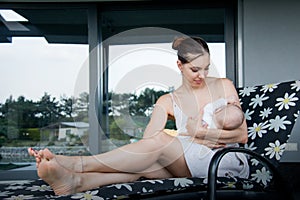 Pretty lady mother breastfeeding her newborn baby sitting at the porch of luxury modern house