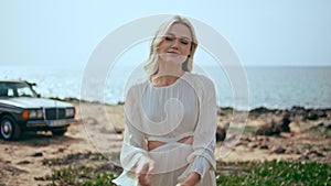 Pretty lady walking coast with retro car on backdrop. Model posing at seashore.