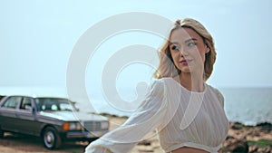 Pretty lady walking coast with retro car on backdrop. Model posing at seashore.