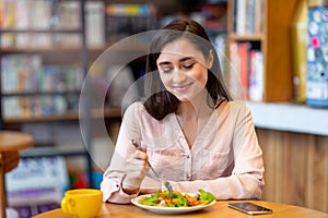 Pretty latin lady tasting fresh healthy salad, sitting at cafe or restaurant in daytime, enjoying delecious lunch