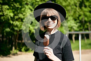 Pretty laughing young girl in sunglasses and hat eating ice cream in the park, photography for blog or ad