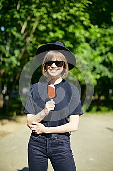 Pretty laughing young girl in sunglasses and hat eating ice cream in the park, photography for blog or ad