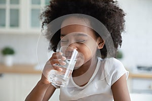 Pretty little African American girl drinking fresh water in kitchen