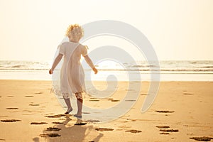 Pretty little baby girl in a white dress long blonde hair relaxing on the beach near sea, summer, vacation, travel