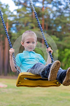 Pretty little blonde boy swinging outdoors on playground