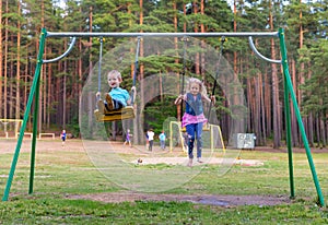 Pretty little blonde girl and boy swinging outdoors on playground