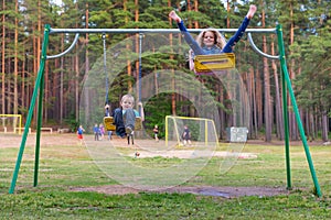 Pretty little blonde girl and boy swinging outdoors on playground