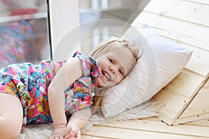 Pretty little blonde girl laughs and lies on white pillow