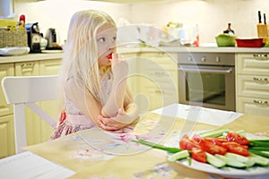 Pretty little blonde girl sits at table and eats photo