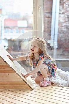 Pretty little blonde girl squats near big window