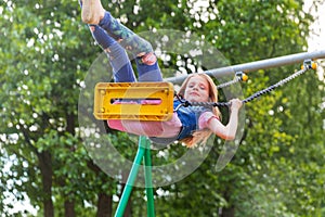 Pretty little blonde girl swinging outdoors on playground