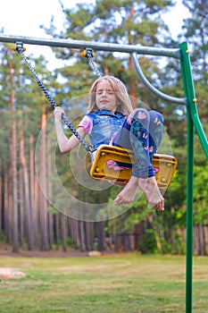 Pretty little blonde girl swinging outdoors on playground