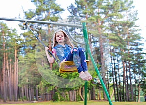 Pretty little blonde girl swinging outdoors on playground
