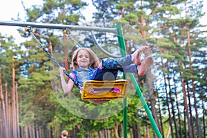 Pretty little blonde girl swinging outdoors on playground