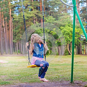 Pretty little blonde girl swinging outdoors on playground