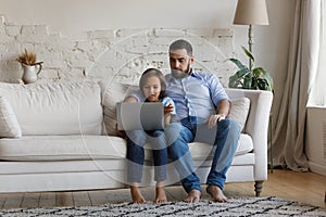 Pretty little boy his father sit on sofa using laptop