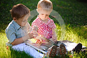 A pretty little boys reading a book on a green grass.