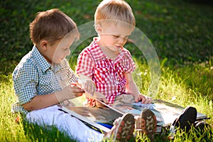 A pretty little boys reading a book on a green grass.