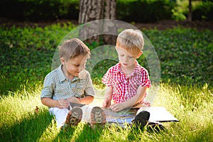 A pretty little boys reading a book on a green grass.