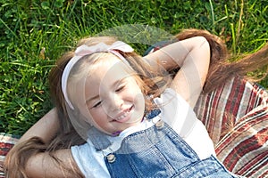 Pretty little child girl with closed eyes laying down on blanket on green grass in summer taking a nap