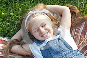 Pretty little child girl with closed eyes laying down on blanket on green grass in summer taking a nap