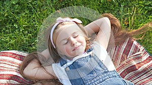 Pretty little child girl with closed eyes laying down on green grass in summer taking a nap.