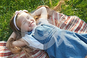 Pretty little child girl with closed eyes laying down on green grass in summer taking a nap