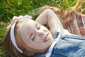 Pretty little child girl laying down on green grass in summer taking a nap