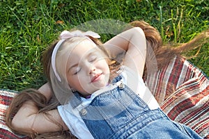 Pretty little child girl laying down on green grass in summer taking a nap