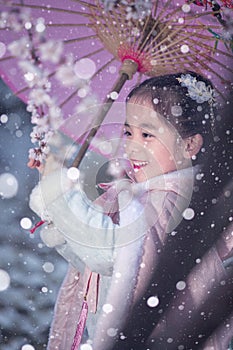 Pretty little Chinese girl in snows, enjoying plum blossom in winter