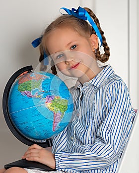 Pretty little European girl kid 6-7 years old holds a world globe in her hand. Distance online learning at home in