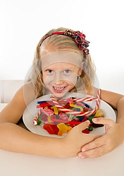 Pretty little female child eating dish full of candy caramel and sweet food in sugar abuse and unhealthy diet