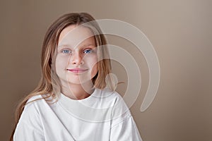 Pretty little girl blue eyes and long blonde hair wears white shirt isolated beige background. Caucasian beautiful