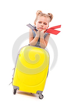 Pretty little girl in blue shirt, white shorts and sunglasses lean on the yellow suitcase and hold red cards and