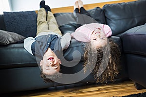 Pretty little girl and boy are lying on their backs on sofa