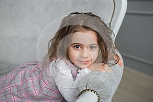 Pretty little girl with brown hair sits on a grey sofa