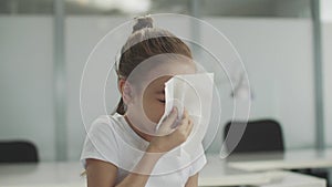 A pretty little girl child picks up a white napkin from the table and blows her nose into it