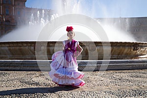 A pretty little girl dancing flamenco dressed in a white dress with pink frills and fringes in a famous square in seville, spain. photo