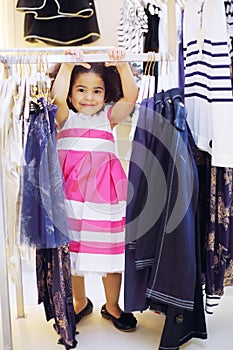 Pretty little girl in dress stands near clothes