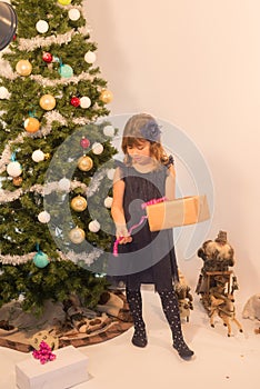pretty little girl in a dress waiting at the foot of the Christmas tree for the opening of presents