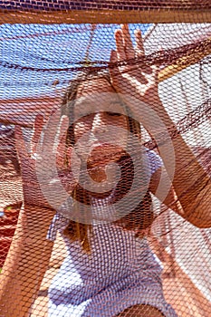 Pretty little girl dressed in a white and blue striped dress locked in a net covered cage. Isolation concept