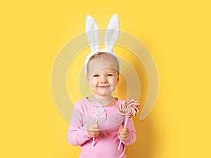 Pretty little girl easter bunny with lollipop or candy on yellow