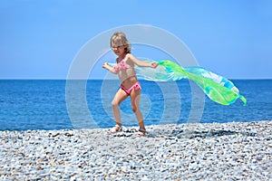 Pretty little girl with fabric on stony seacoast