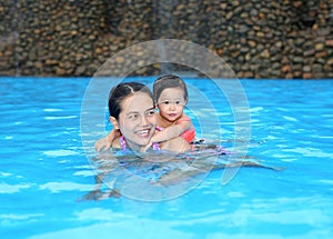 Pretty little girl with her mother playing in swimming pool outdoors