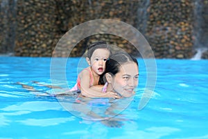 Pretty little girl with her mother playing in swimming pool outdoors