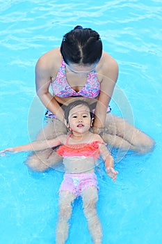 Pretty little girl with her mother playing in swimming pool outdoors