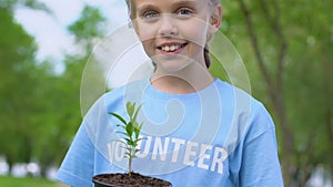 Pretty little girl holding plant sapling and smiling on camera, eco volunteering